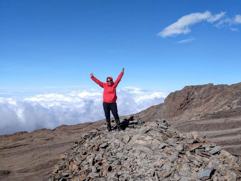 Laurel at the top of a mountain with clouds at the background, for the kilimanjaro hiking tour day 6