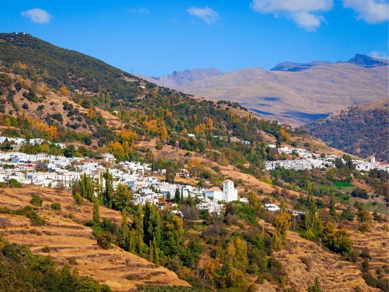 A white Alpujarras village spread along a terraced hillside with the Sierra Nevada ridges behind it in southern Spain