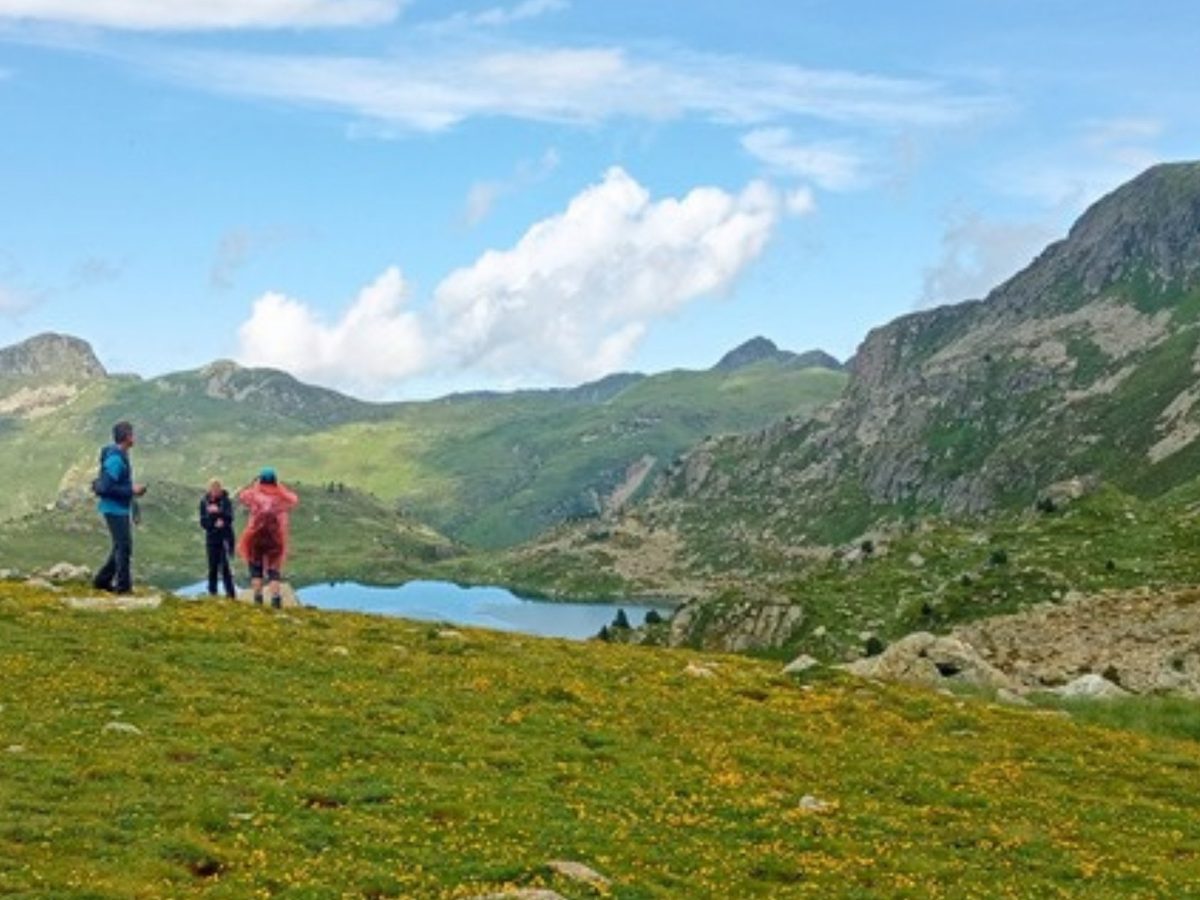 Three hikers looking down on a high mountain lake while hiking in Andorra