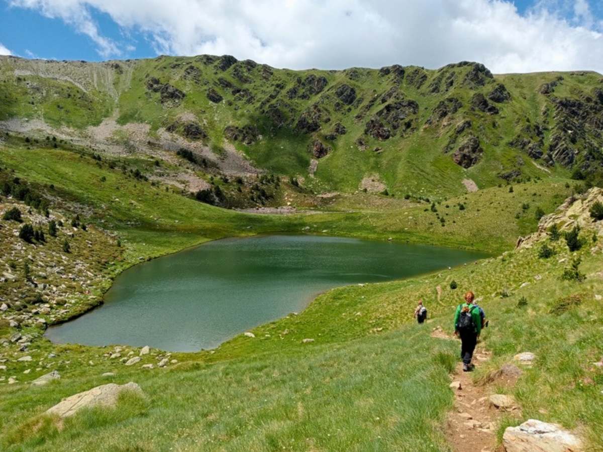 Hiker on the trail down to a green high mountain lake on a self-guided Andorra hiking tour in the Pyrenees