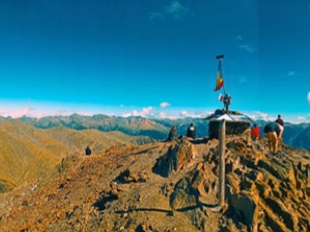 Hikers at the summit marker on a peak in the Pyrenees at sunset on an Andorra hiking tour
