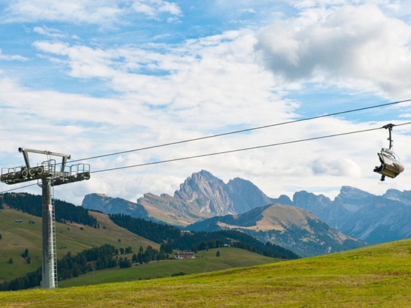 The Alpe di Siusi cable car crossing above the meadows with the Dolomite peaks behind, South Tyrol, Italy