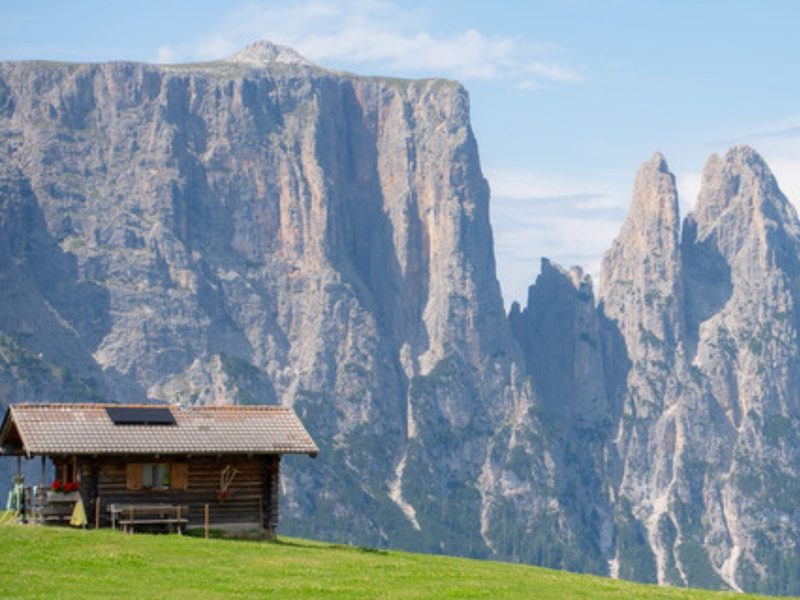 A wooden chalet on the meadow below the Sciliar cliffs, where the Alpe di Siusi hotels sit on the plateau, South Tyrol, Italy