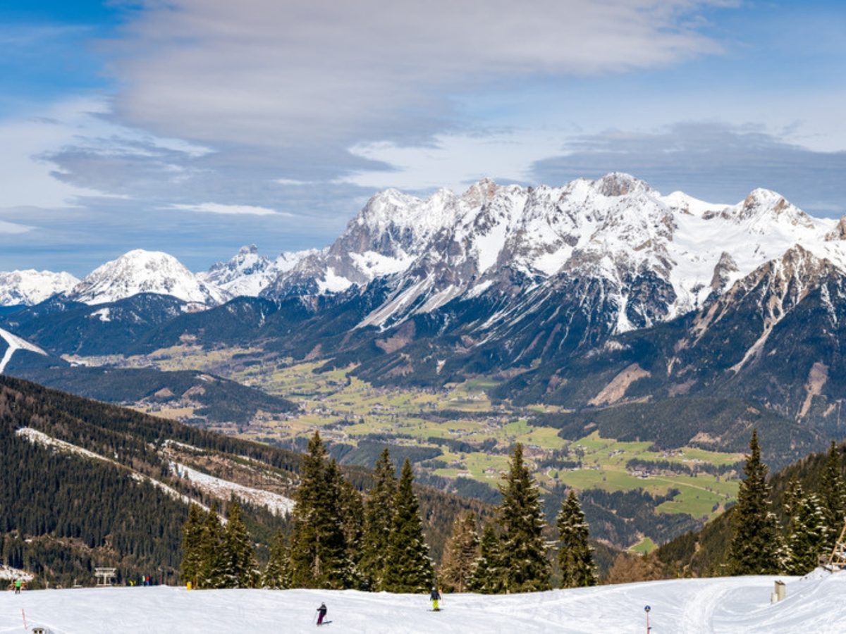 Skier on a slope above the Enns valley with the Dachstein range behind, a view from the ski area near the chalets in Schladming