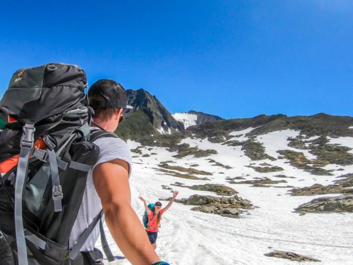 Hikers crossing late-lying snow on a sunny day in the mountains around Schladming, a summer reason to book one of the chalets in Schladming