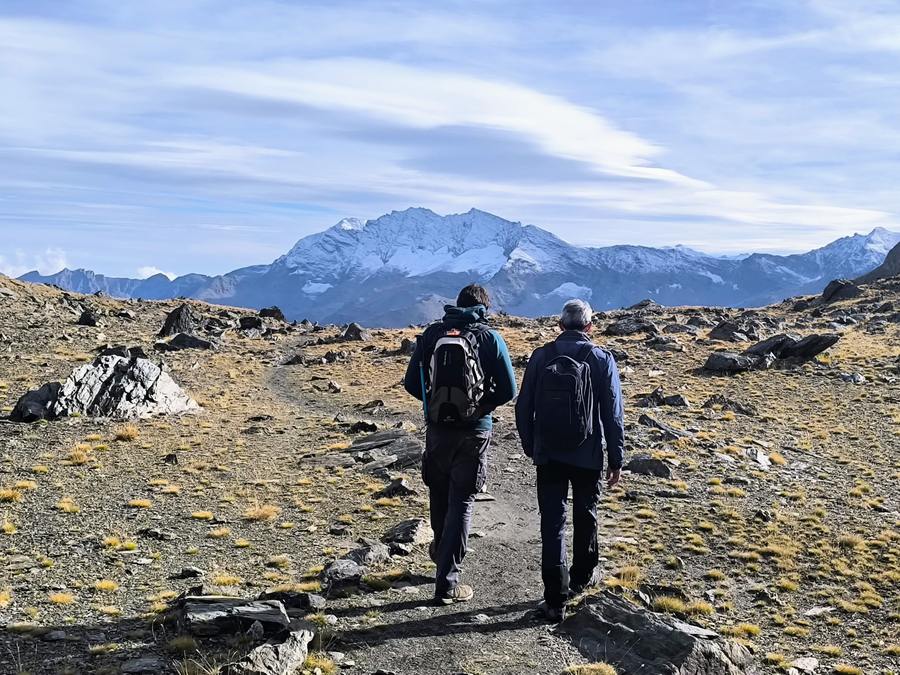 Two hikers on the Gran Paradiso hiking tour heading along a high trail towards a snow-capped peak in the Italian Alps