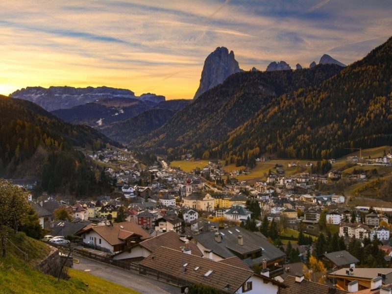 Hotels and rooftops of Ortisei at sunset below Sassolungo in Val Gardena, Dolomites, Italy