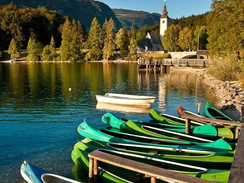 Wooden boats drawn up on the shore of Lake Bohinj beside the old stone church, at the end of the Slovenia hut to hut hike