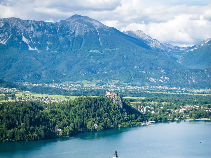 Lake Bled from above, with Bled Castle on its cliff and the mountains beyond, the viewpoint you hike to on day 5 of guided hiking in the Slovenian Alps
