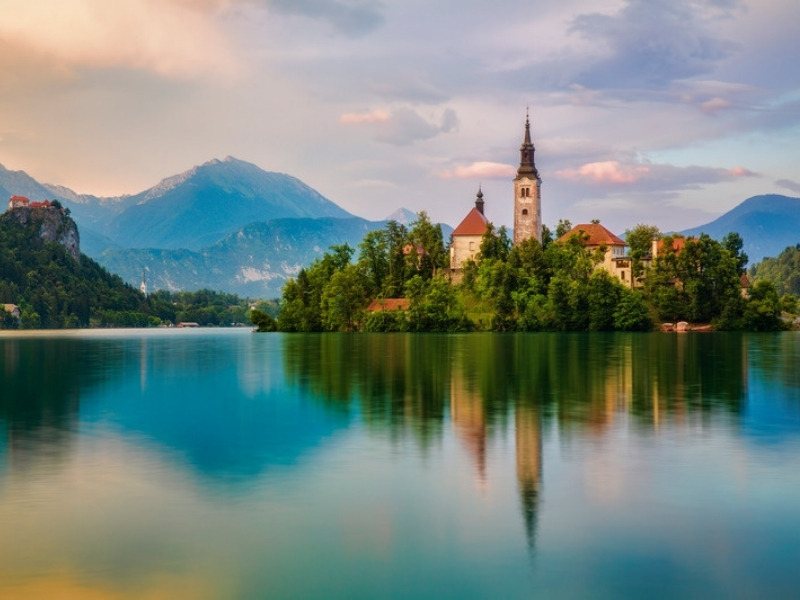 Lake Bled at dawn with the island church reflected in mirror still water and the castle on the cliff, the last two nights of the Slovenia hut to hut tour
