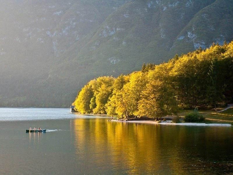 Autumn trees reflected in Lake Bohinj with a rowing boat on the water, inside Triglav National Park