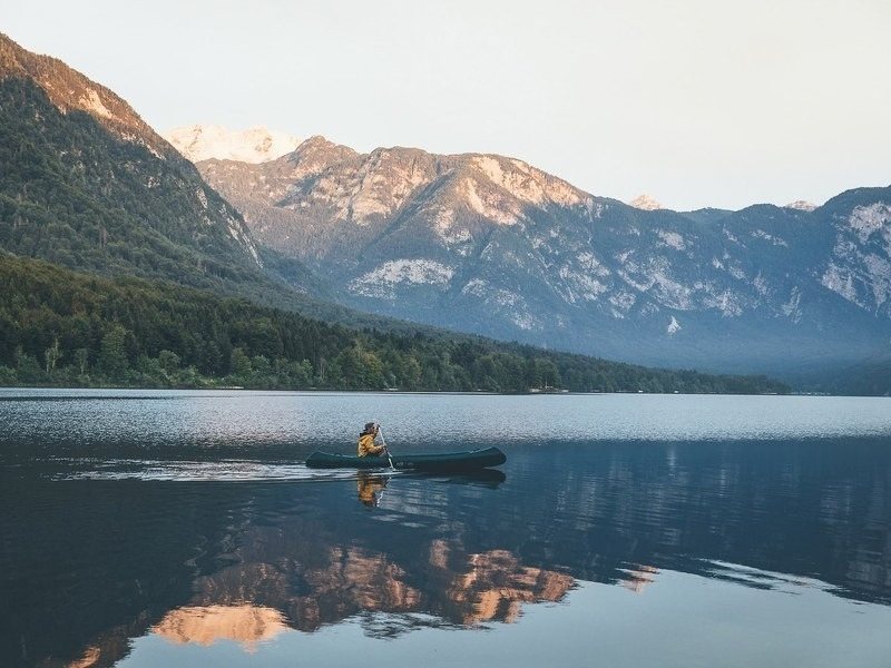A canoe on the still water of Lake Bohinj with the Julian Alps behind, where the hut to hut hike finishes with a swim