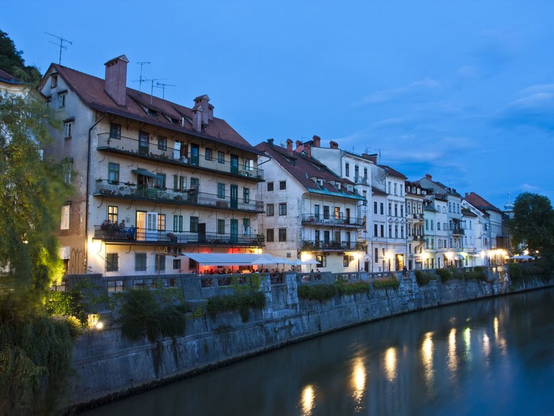 Pastel townhouses and lit cafe terraces along the Ljubljanica river in Ljubljana old town, where our Slovenia hiking tour starts and finishes