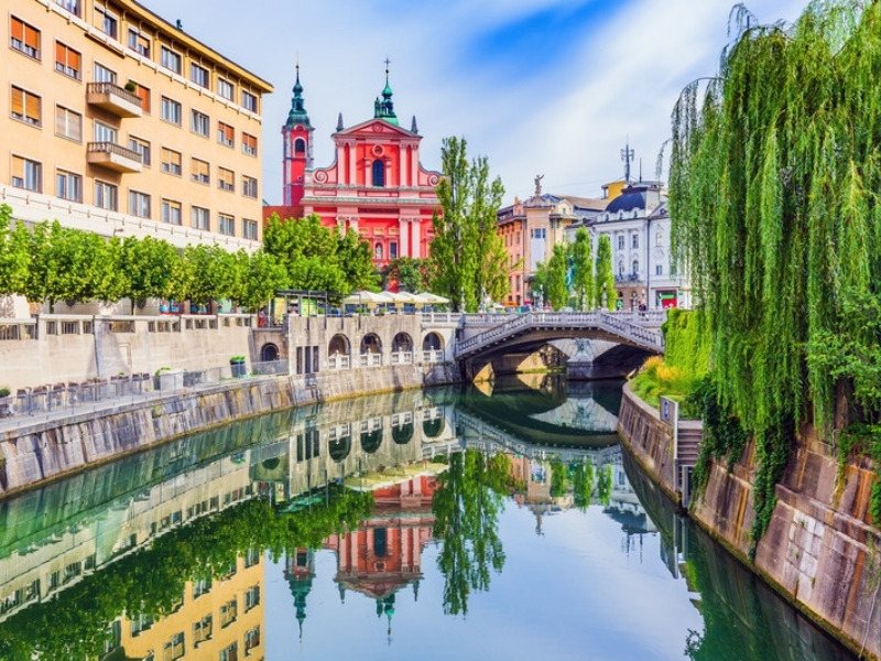 The Ljubljanica river in Ljubljana old town with the Triple Bridge, the pink Franciscan church and willows on the bank, where the Slovenia hut to hut hiking tour starts