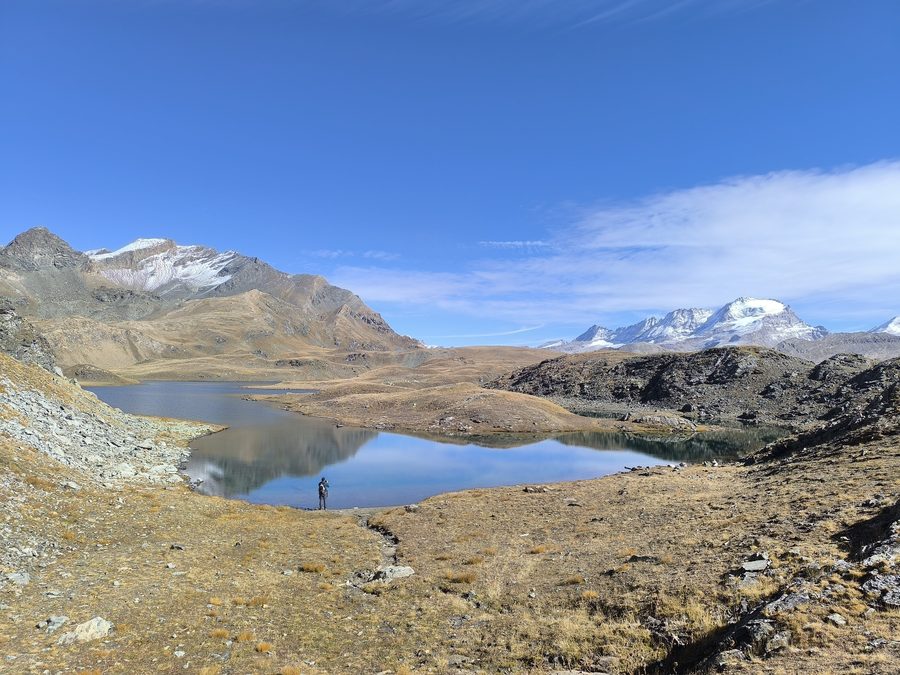 A lone hiker beside a still glacial lake on the Plan del Nivolet, Gran Paradiso National Park
