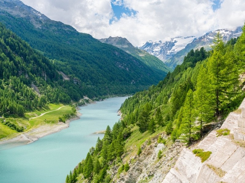The turquoise lake and larch forest of the Valgrisenche below glaciated peaks on the Gran Paradiso hiking tour in the Italian Alps