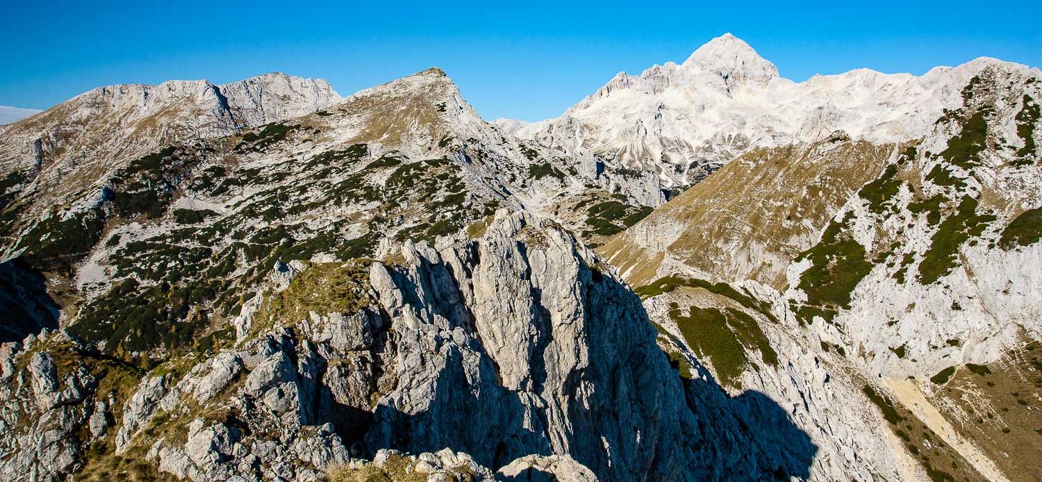 The high ridges of Slovenia's Julian Alps under deep blue sky, with the white summit massif of Mt. Triglav behind, on our self-guided hut to hut hiking tour